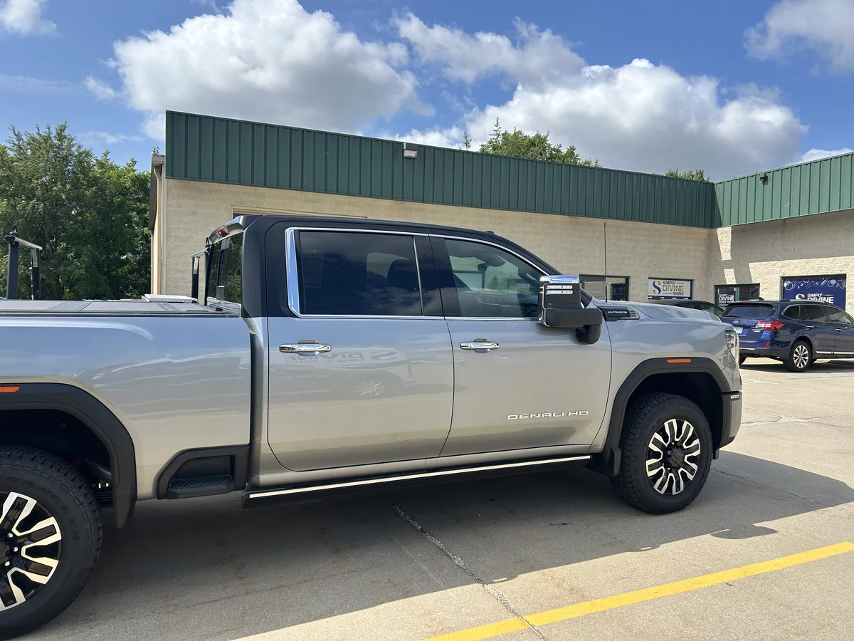 Finished: side profile of the Lighthouse GMC Sierra HD Denali Ultimate showing the satin-black upper cab and A/B/C pillar treatment against the retained factory silver body panels, photographed outside the Simply Divine Signs & Wraps shop in Bloomington, IL.