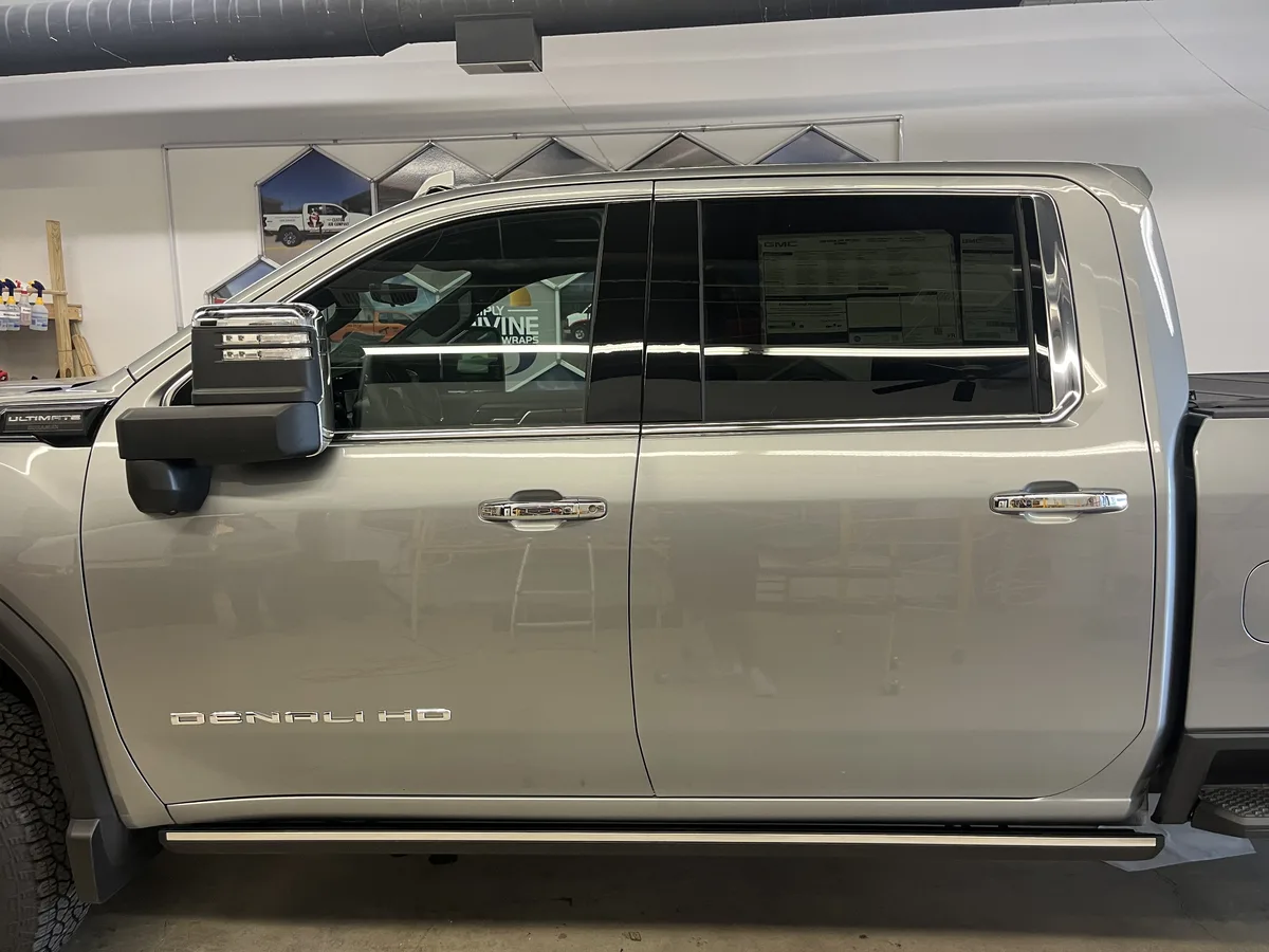 Before: passenger-side view of the 2026 GMC Sierra 2500 HD Denali Ultimate in the Simply Divine Signs & Wraps install bay prior to the tuxedo wrap — factory silver paint, factory-tinted glass, and factory chrome and trim visible.