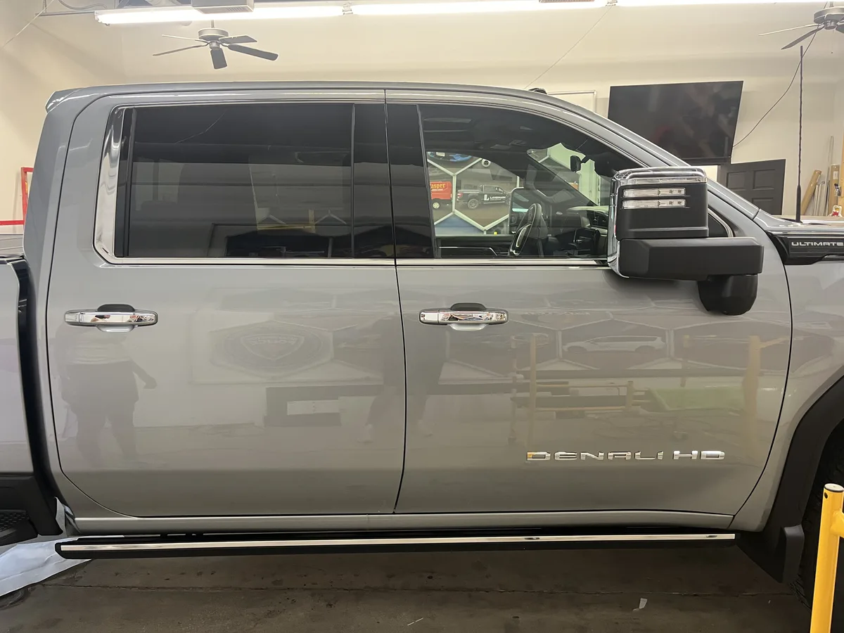 Before: driver-side view of the 2026 GMC Sierra 2500 HD Denali Ultimate in the Simply Divine Signs & Wraps install bay before the satin-black upper-cab and pillar wrap was installed.