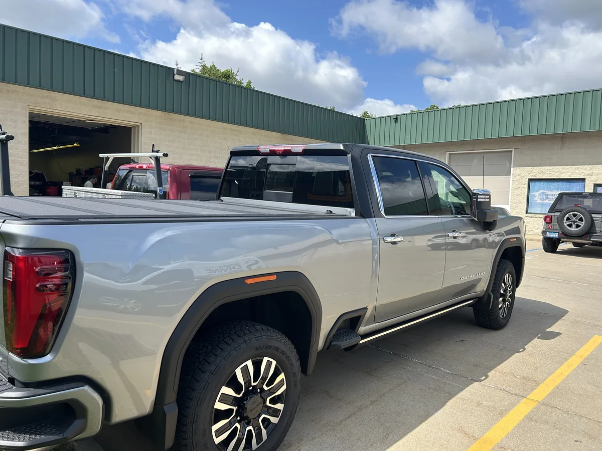 Finished: rear three-quarter view of the Lighthouse GMC Sierra 2500 HD Denali Ultimate tuxedo wrap — satin-black roof and cab surround with factory silver bed and Denali HD chrome trim retained.
