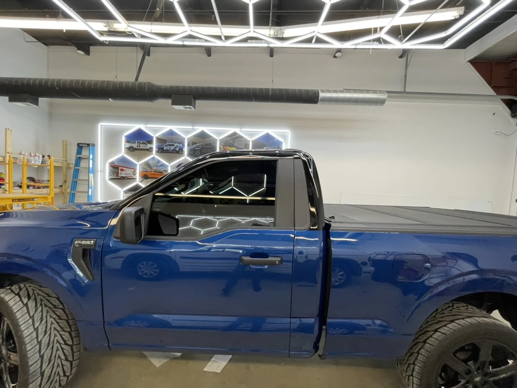 A blue Ford F-150 with a black roof, photographed inside the shop.
