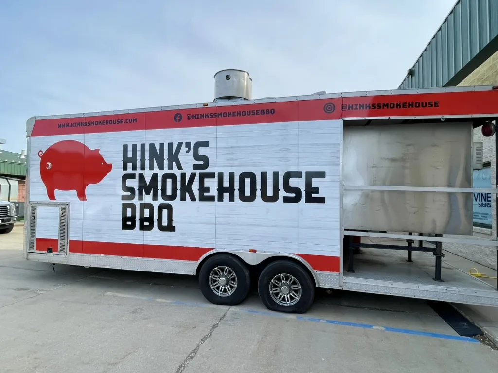 Hink's Smokehouse BBQ 25-foot food trailer with a white barn wood wrap, red band, and red pig mark, Bloomington, IL.