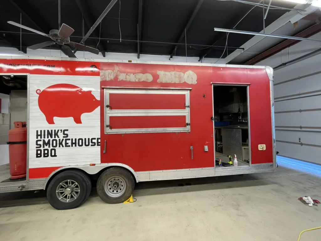 The trailer with the previous wrap removed and a temporary Hink's Smokehouse panel in place before the new wrap.