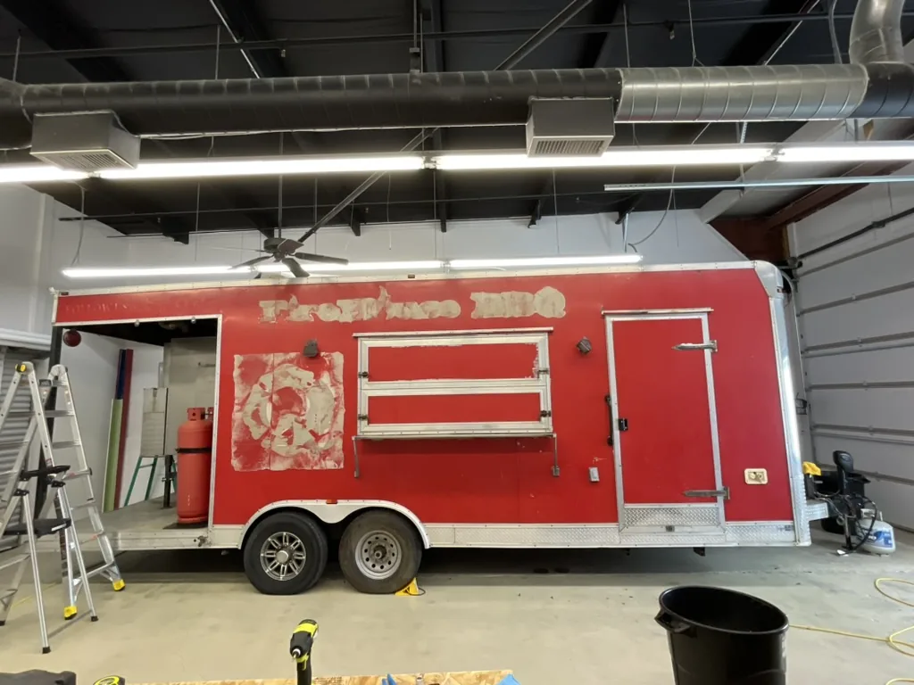 The trailer stripped to red paint with adhesive residue and ghosting where the previous wrap had been.