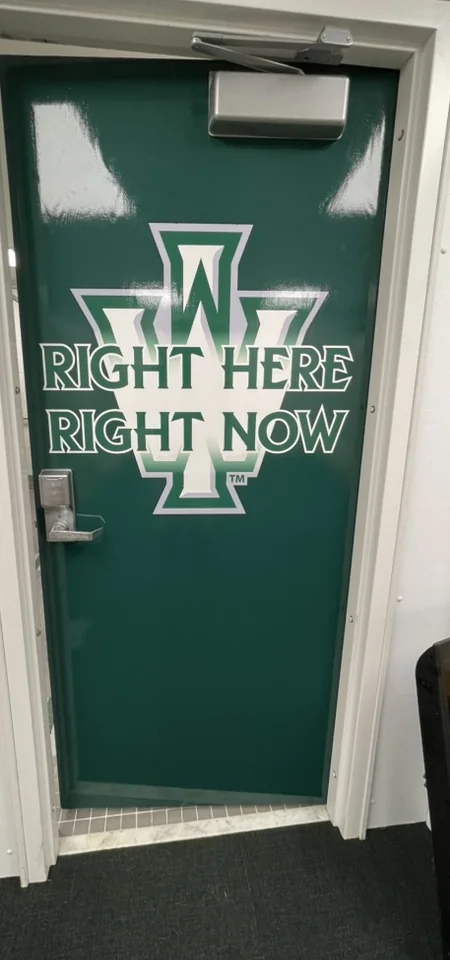 Illinois Wesleyan flag football locker room door graphic reading Right Here Right Now, Bloomington, IL.