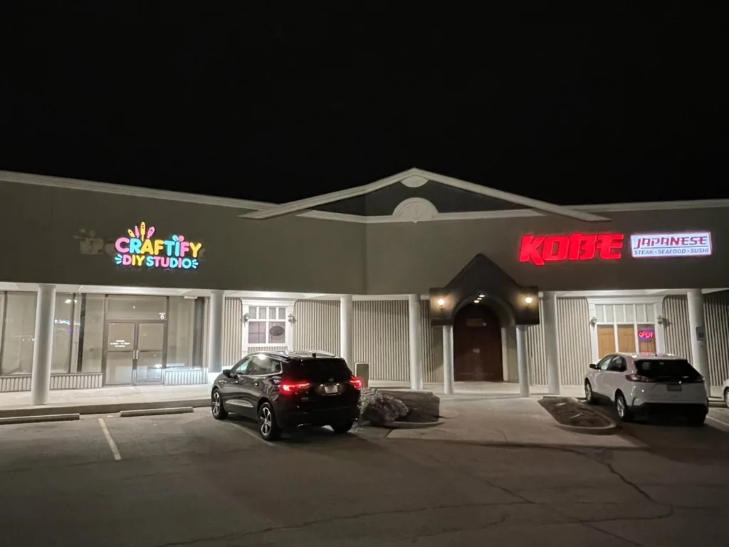 Lighted signs for Kobe Japanese Steak House and Craftify DIY Studio glowing at night on a shared building in Bloomington, IL.