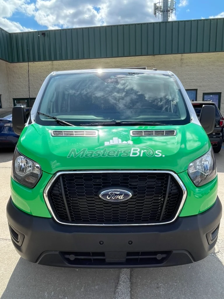 Front of the Ford Transit, with the hood in green carrying the Masters Bros. logo.