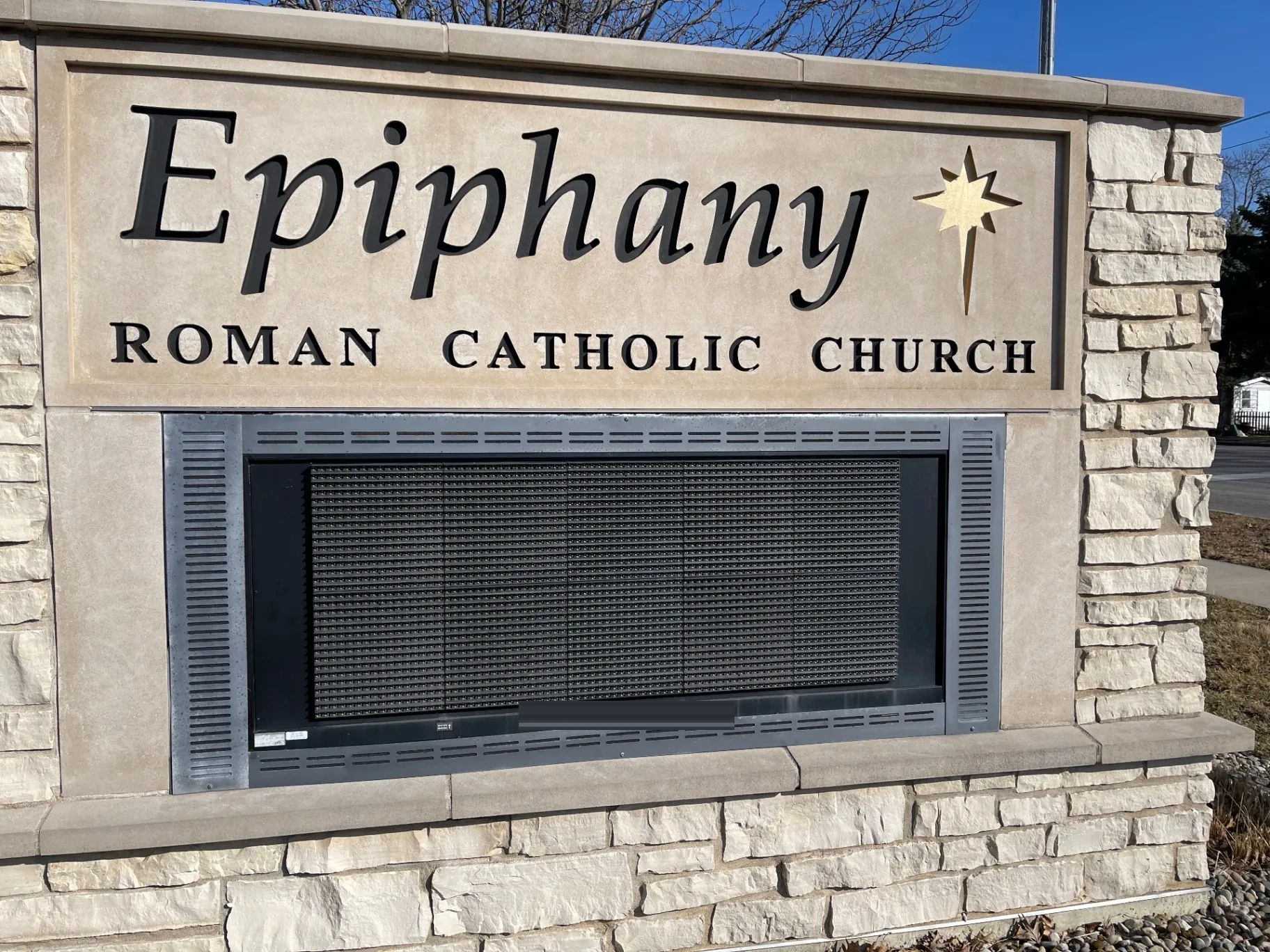 The same stone monument before the work. The old display sits dark in the opening and is visibly smaller than it, with grey surround and vent strips showing above, below, and on both sides.