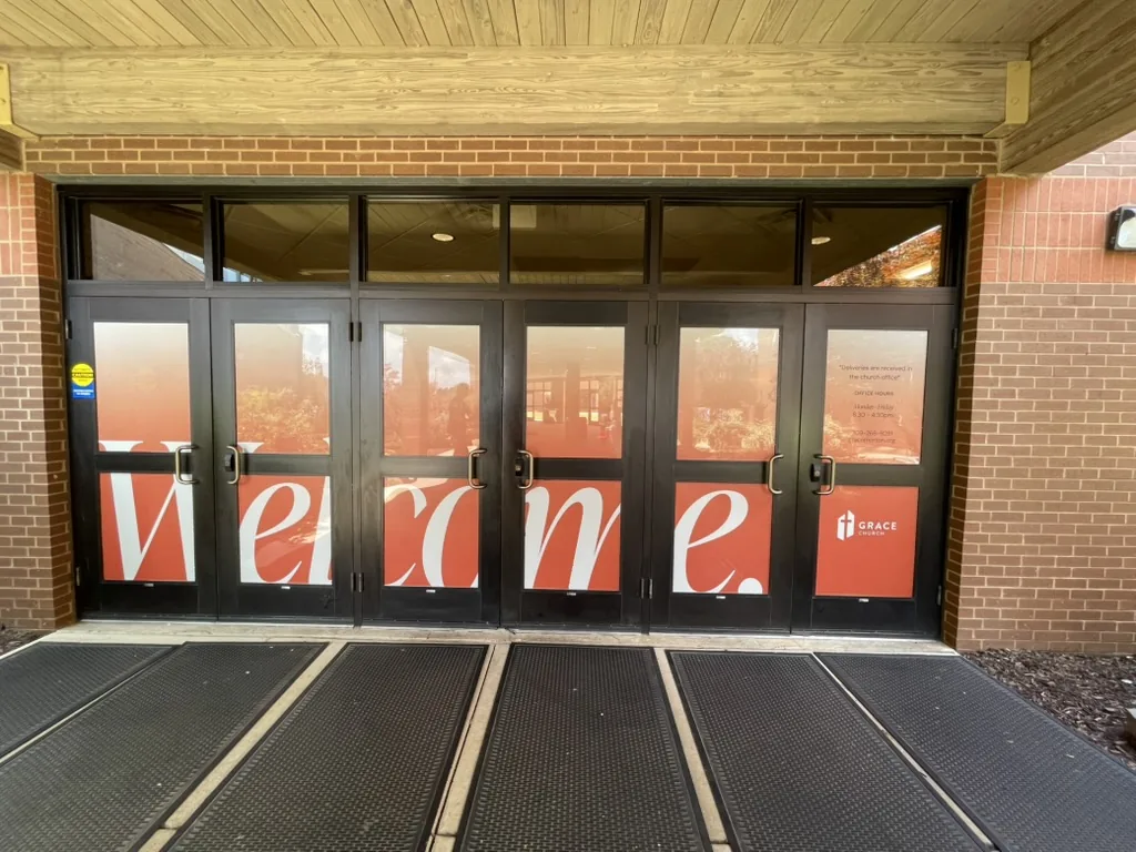A main entrance after the work. One Welcome runs across all six doors, and the right-hand door lists the church office hours.
