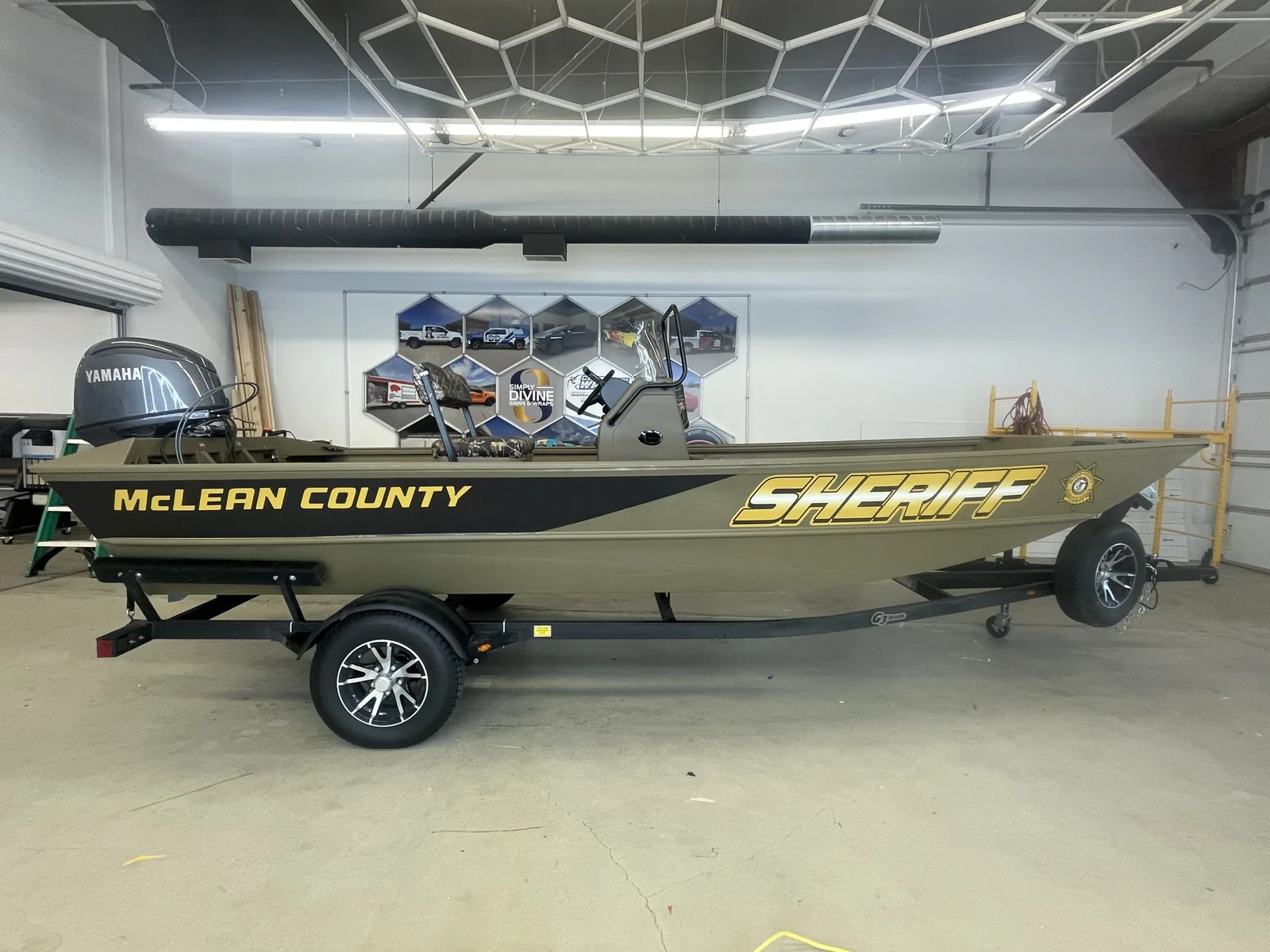 The Sheriff's patrol boat in our shop, sitting on its trailer, with gold SHERIFF lettering and the county star on the hull and McLEAN COUNTY along the bow.